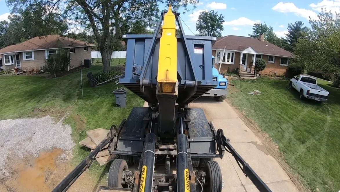Roll-off truck lowering a dumpster onto a residential driveway