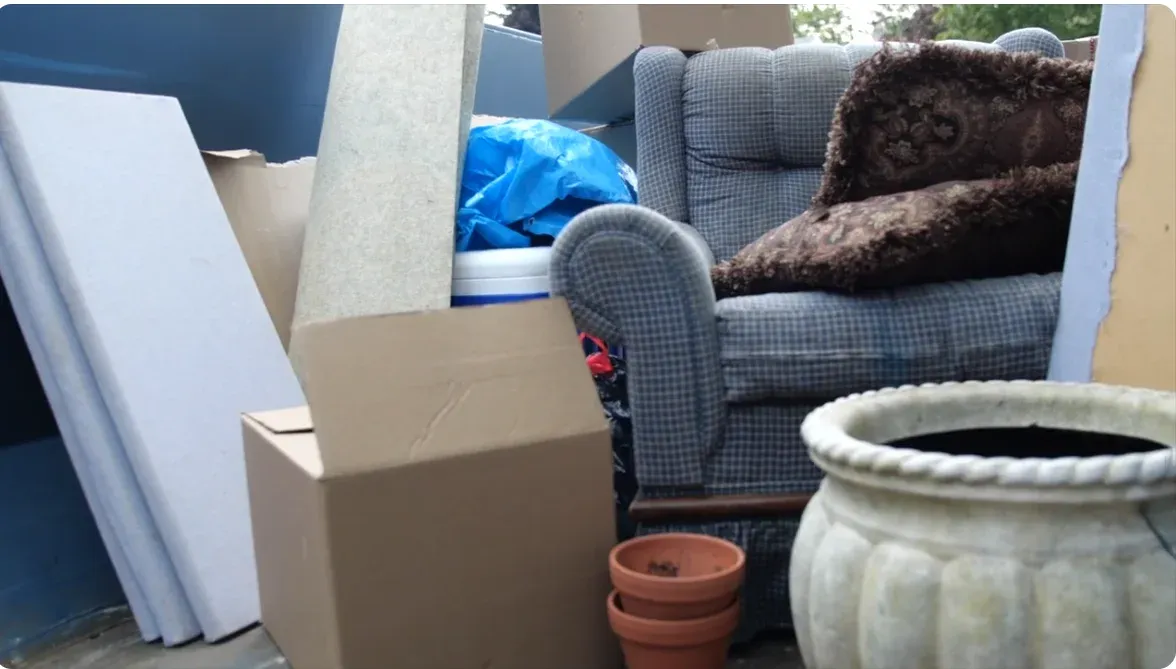 Household cleanout debris in a roll-off dumpster: armchair, boxes, cushions and planters