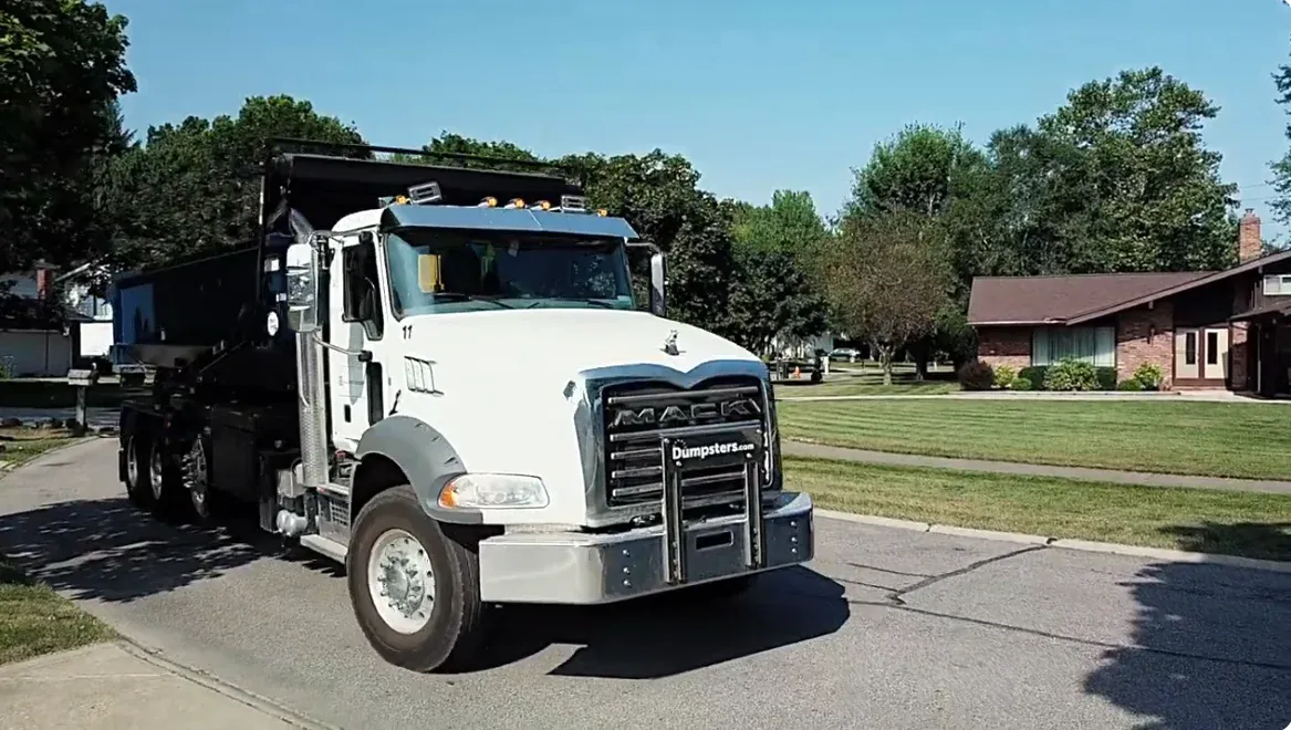 Roll-off dumpster truck arriving on a residential street for a driveway delivery