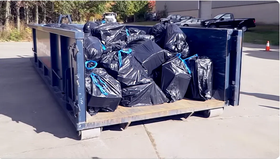 Roll-off dumpster loaded with black trash bags from a cleanout, below the top edge